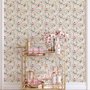 Pink wallpaper with watercolour blush, coral and yellow wildflowers, sage leaves and stems on a warm cream-white ground.