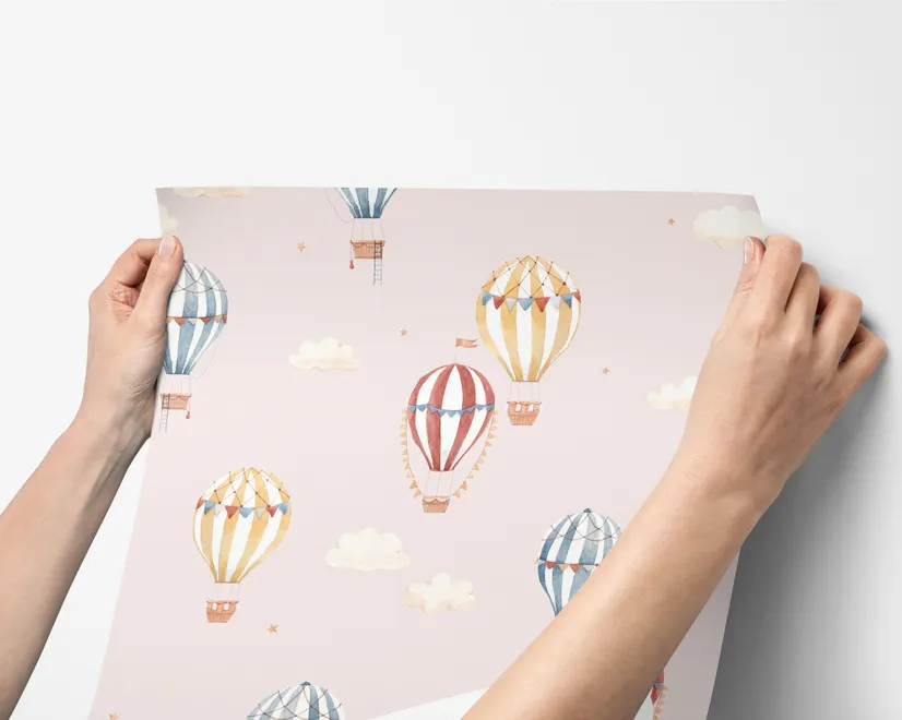 Hot air balloon nursery room wallpaper with watercolour balloons, clouds and stars on a soft blush-pink ground
