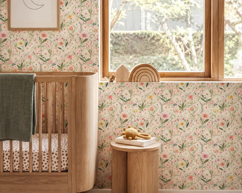 Pink wallpaper with watercolour blush, coral and yellow wildflowers, sage leaves and stems on a warm cream-white ground.